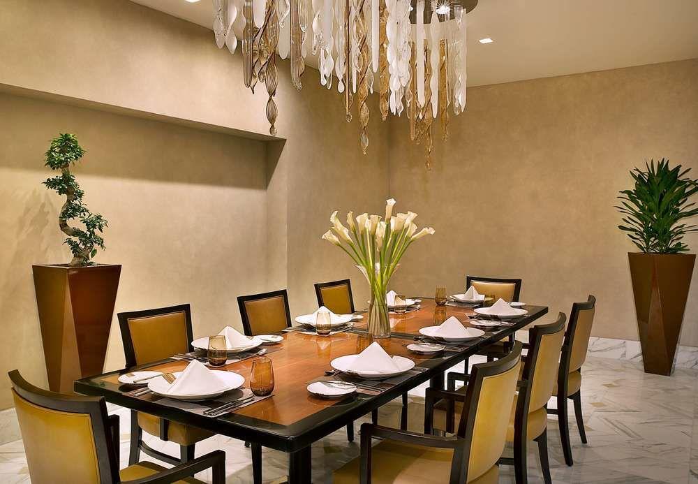 자발 오마르 메리어트 호텔, 마카 메카 외부 사진 The photo shows an elegant dining room featuring a long wooden table with seating for several people. The table is set with white plates, napkins, and glasses. In the center, there is a tall vase filled with fresh flowers. The room has light, warm-co