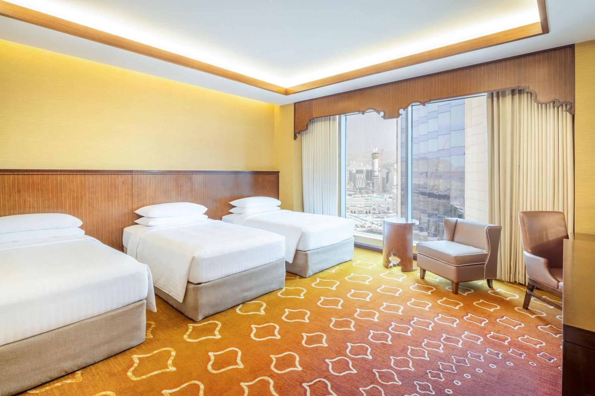 자발 오마르 메리어트 호텔, 마카 메카 외부 사진 The photo depicts a hotel room featuring three beds arranged in a neat manner. The walls are painted a soft yellow, and there is a decorative wooden panel behind the beds. The carpet has a unique orange design, contributing to a warm atmosphere. Larg